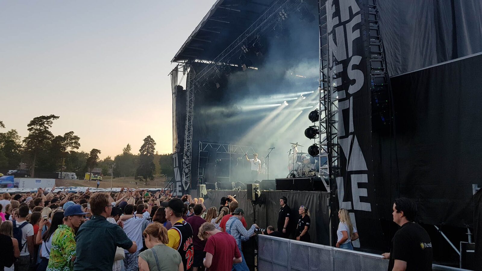 Scenen på Stavernfestivalen i kveldssol, med publikum foran og sikkerhetsvakter langs gjerdet.